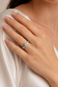 A close-up of a woman's hand wearing a silver-toned diamond ring, resting on her shoulder against a soft cream satin top.