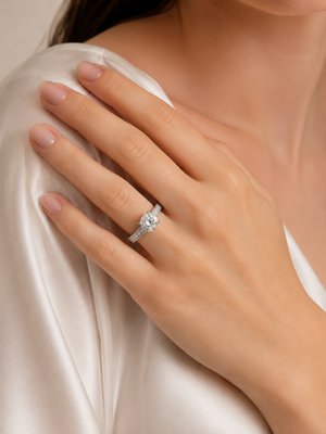 A close-up of a woman's hand wearing a silver-toned diamond ring, resting on her shoulder against a soft cream satin top.